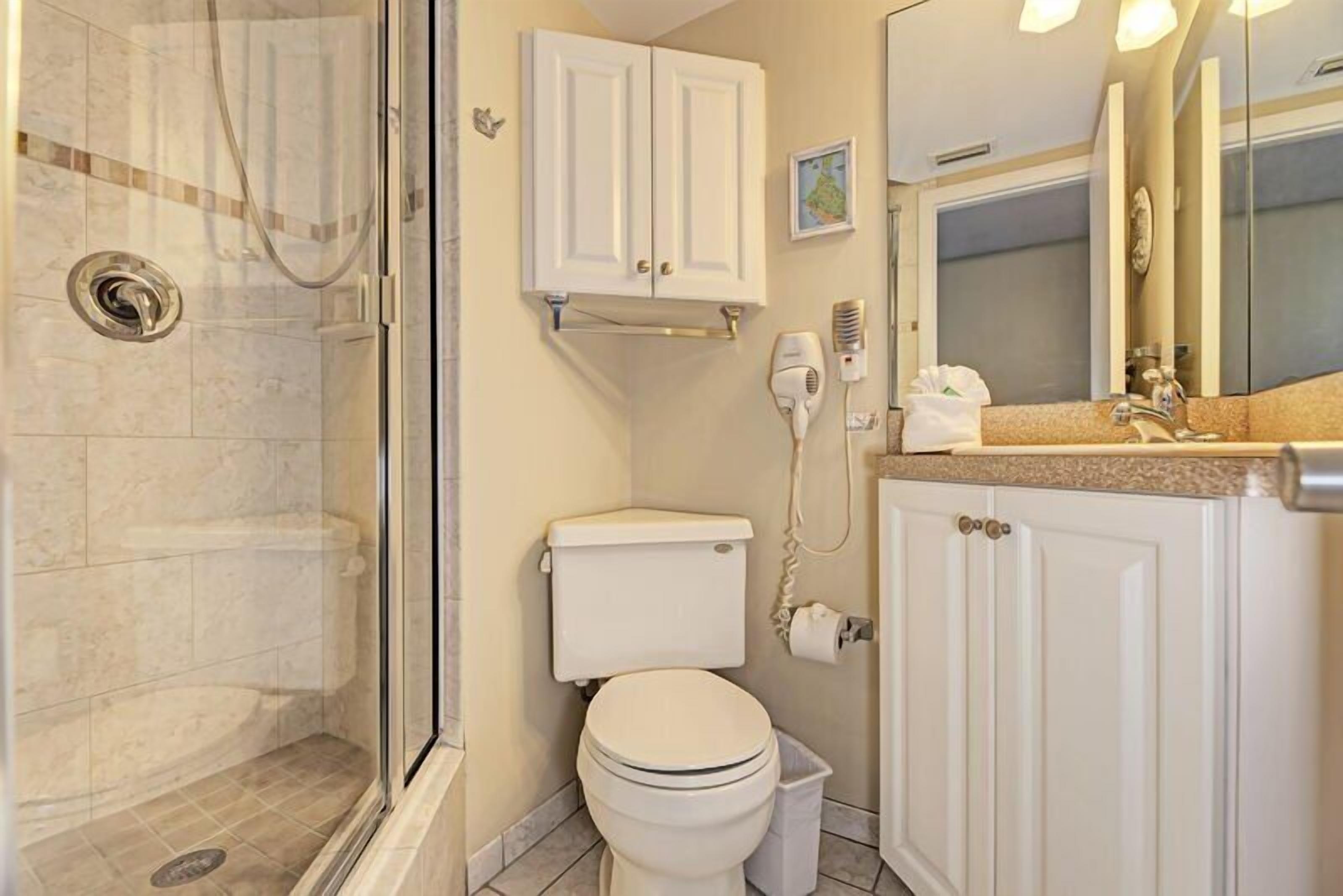 A bathroom with a glass-enclosed shower, a toilet, a sink with a vanity, and a mirror.