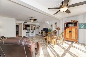 A spacious living room with a fireplace, a dining area with wooden chairs, and a kitchen in the background.