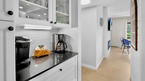 A modern kitchen with white cabinetry, a coffee maker, and a basket on the counter.