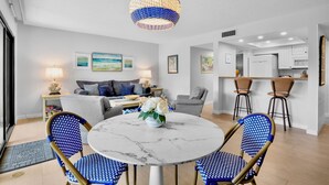 A modern living room with a round marble table, blue patterned chairs, a grey sofa, and a hanging light fixture.