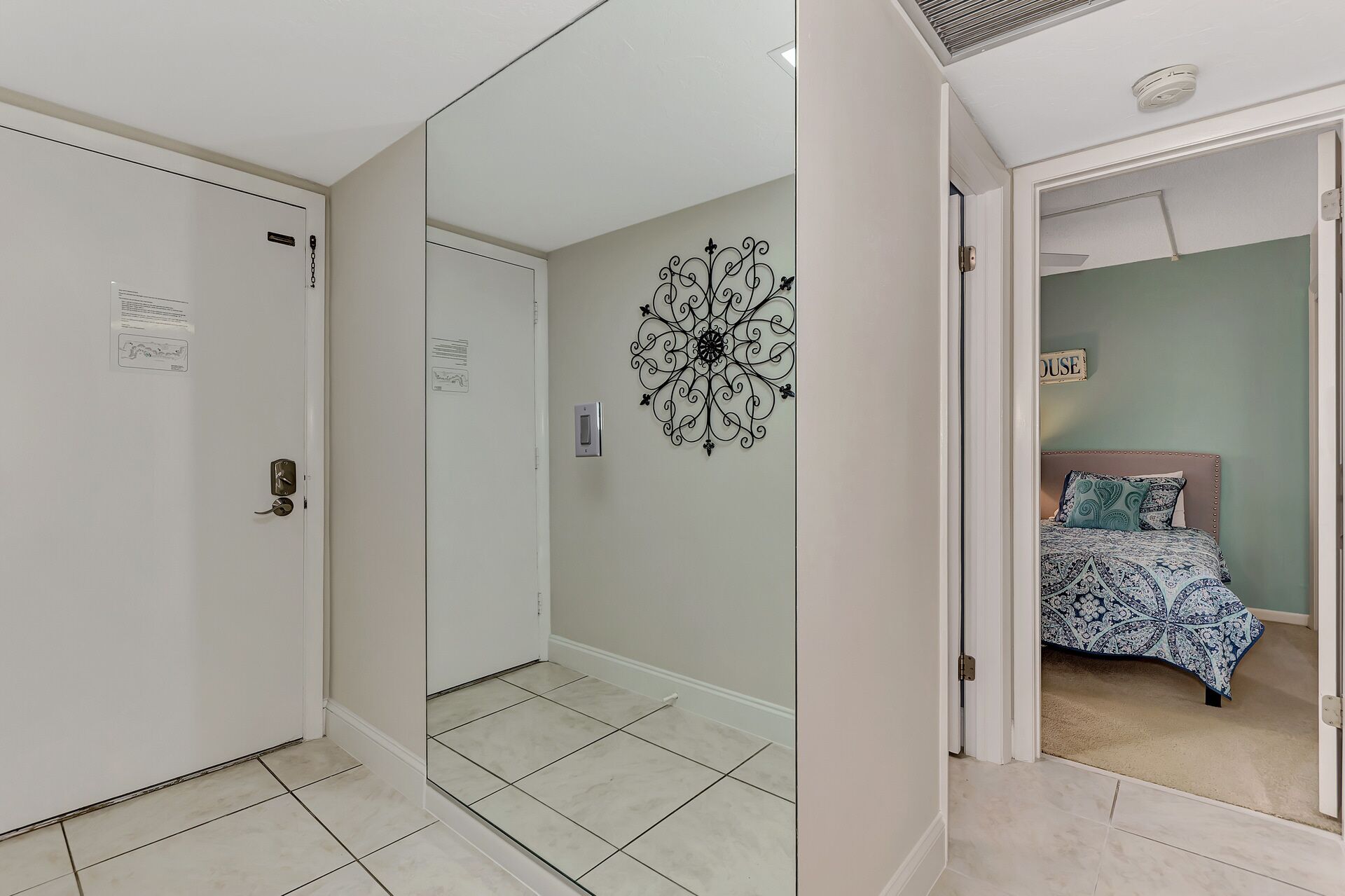 A room with a bed, a wall-mounted decorative item, and a door with a sign.