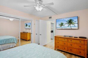 A bedroom with a bed, a dresser, a ceiling fan, and a painting of a beach scene. - Midnight Cove II 510F - Siesta Key Beach Condo Rental with Community Amenities (Siesta Key)