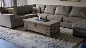 A living room with a sectional sofa, a coffee table, and a painting of a beach scene.