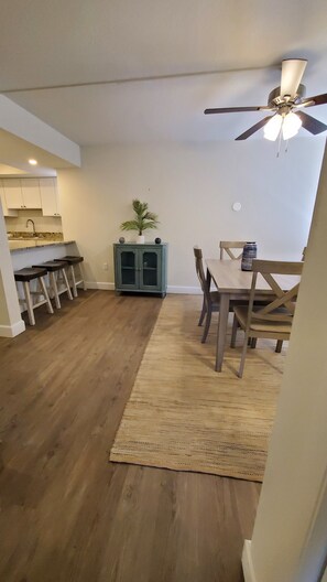 A spacious living area with a dining table and chairs, a ceiling fan, and a kitchen area with stools. - Midnight Cove II 520 D: 2-Bedroom Townhouse Steps from Crescent Beach! (Siesta Key)