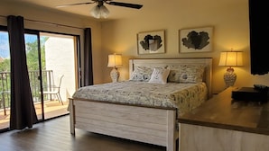 A spacious bedroom with a large bed, ceiling fan, and a balcony with a chair.