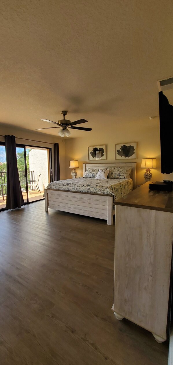A spacious bedroom with a large bed, ceiling fan, and a balcony with a chair. - Midnight Cove II 520 D: 2-Bedroom Townhouse Steps from Crescent Beach! (Siesta Key)