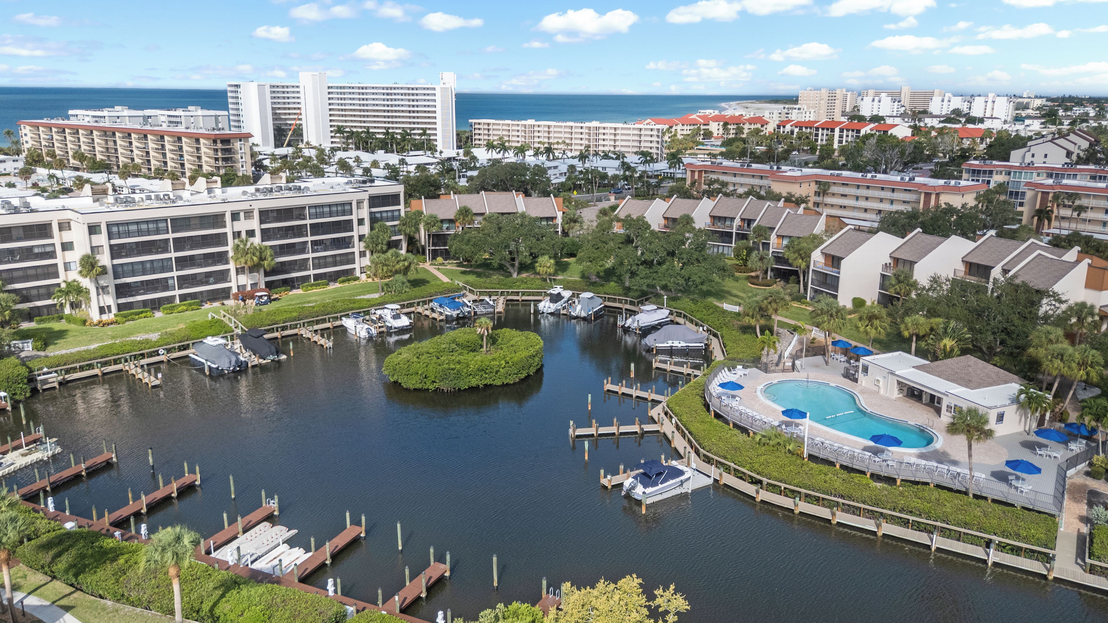 A marina with boats docked, a central island, and a swimming pool area with lounge chairs.