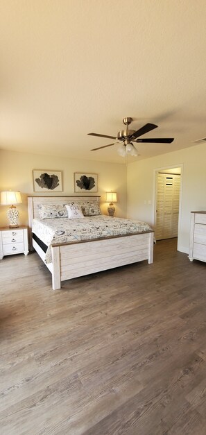 A bedroom with a wooden bed, two bedside tables with lamps, a ceiling fan, and a door with shutters. - Midnight Cove II 520 D: 2-Bedroom Townhouse Steps from Crescent Beach! (Siesta Key)