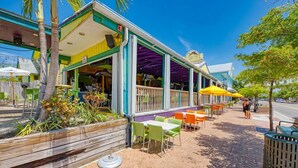 An outdoor cafe with a covered seating area, wooden planters, and a clear sky. - Midnight Cove II 524D: 3-Bedroom Townhouse Steps from the Pool in Siesta Key (Siesta Key)