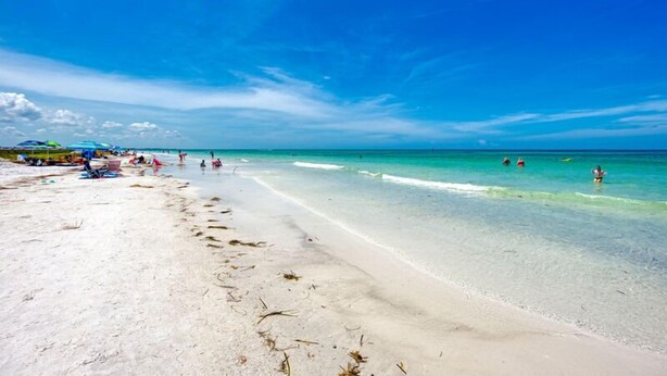 A beach with clear turquoise water, a sandy shore, and a few umbrellas. - Midnight Cove II 524D: 3-Bedroom Townhouse Steps from the Pool in Siesta Key (Siesta Key)