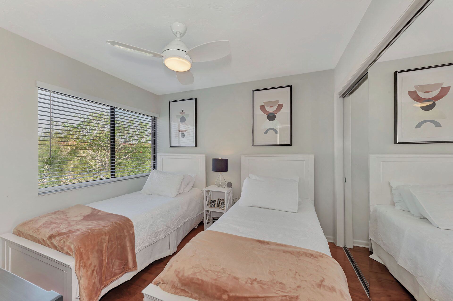 A bedroom with two single beds, a ceiling fan, and a window with blinds.