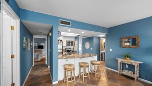 A modern kitchen with a central island, bar stools, and a decorative console table. - Midnight Cove II 611F: Ground-floor Bayside Condo with Access to Pool and Beach (Siesta Key)