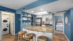 A modern kitchen with a central island, built-in appliances, and a laundry area. - Midnight Cove II 611F: Ground-floor Bayside Condo with Access to Pool and Beach (Siesta Key)