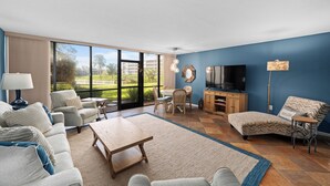 A spacious living room with a large TV, comfortable seating, and a view of the outdoors. - Midnight Cove II 611F: Ground-floor Bayside Condo with Access to Pool and Beach (Siesta Key)