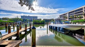 A marina with docked boats, a wooden pier, and a building with multiple floors in the background. - Midnight Cove II 820F - Updated Siesta Key Bayside Rental, Pool and Tennis Acces (Siesta Key)