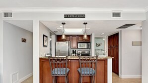 A kitchen with a central island, two bar stools, a refrigerator, a microwave, and a sink. - Midnight Cove II 820F - Updated Siesta Key Bayside Rental, Pool and Tennis Acces (Siesta Key)