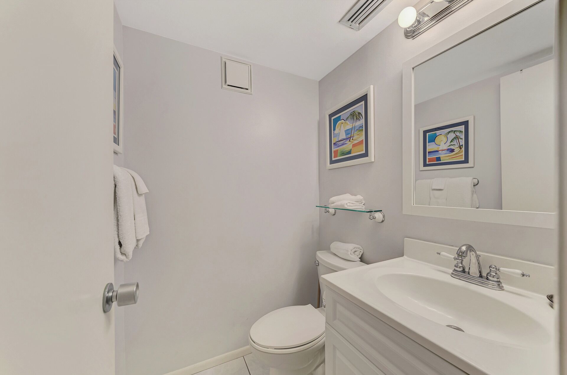 A bathroom with a toilet, sink, and shower. There are two framed pictures on the wall.