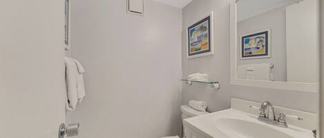A bathroom with a toilet, sink, and shower. There are two framed pictures on the wall.