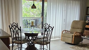 Ein geräumiges Wohnzimmer mit Essbereich, großen Fenstern und Vorhängen, einem Deckenventilator und einem bequemen Sessel.