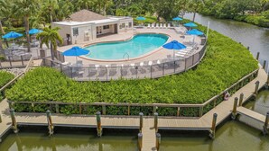 A pool area with a circular pool, lounge chairs, umbrellas, and a wooden deck over water. - Midnight Cove II 833F - Siesta Key Condo with Balcony and Marina View! (Siesta Key)
