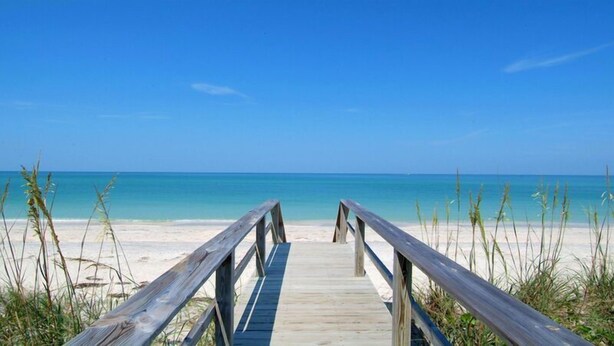 A wooden boardwalk leading to a beach with clear blue water and a sandy shore. - Midnight Cove II 833F - Siesta Key Condo with Balcony and Marina View! (Siesta Key)