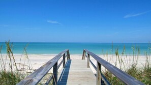 Una passerella di legno che conduce a una spiaggia con acque cristalline e una riva sabbiosa.