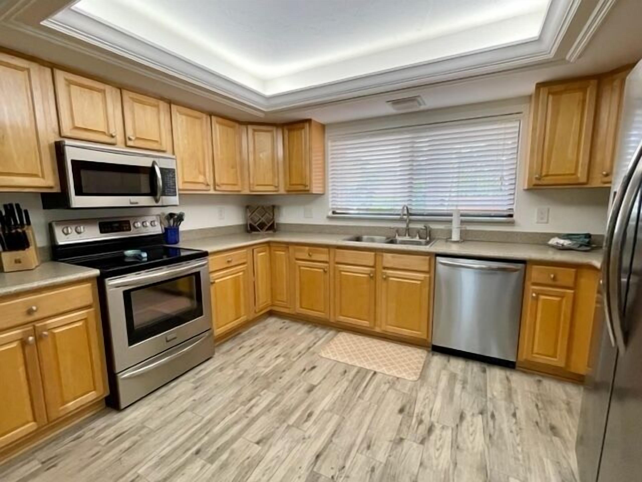 Eine moderne Küche mit Holzausstattung, Edelstahlgeräten und einem Fenster mit Jalousien.