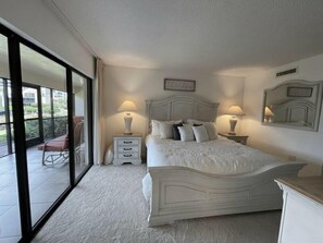 Un dormitorio con una cama grande, dos mesitas de noche, una silla y un ventanal corredero que da a un balcón.