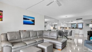 Uma sala de estar moderna com um sofá modular cinza, pufes e uma área de jantar com mesa e cadeiras.