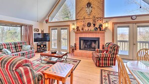 A spacious living room with a fireplace, large windows, and a ceiling fan. - Murphy Cabin w/ Deck and Stunning Mountain Views (Murphy)