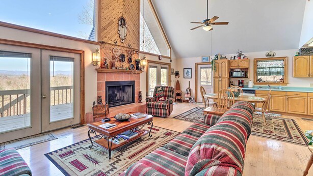 A spacious living room with a fireplace, a large sofa, a television, and a dining area with wooden cabinets. - Murphy Cabin w/ Deck and Stunning Mountain Views (Murphy)