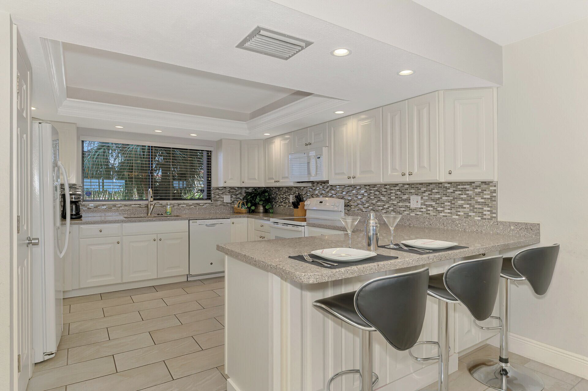 A modern kitchen with white cabinetry, a granite countertop, and a bar area with three stools.
