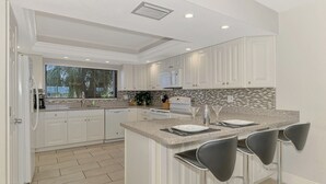 Une cuisine moderne avec des meubles blancs, un plan de travail en granit et un coin bar équipé de trois tabourets.