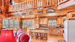 A cabin interior with a wooden interior, a red sofa, a kitchen with wooden cabinets, and a dining area. - Murphy Cabin: Wheelchair Accessible w/ Fire Pit! (Murphy)