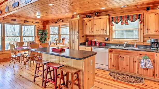 A wooden cabin kitchen with a central island, bar stools, and a dining area with chairs. - Murphy Cabin: Wheelchair Accessible w/ Fire Pit! (Murphy)