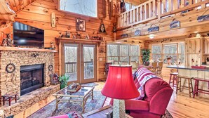 A cozy cabin interior with a stone fireplace, a red lamp, a red sofa, and a dining area with wooden furniture. - Murphy Cabin: Wheelchair Accessible w/ Fire Pit! (Murphy)