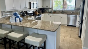 Eine moderne Küche mit weißen Schränken, Granit-Arbeitsplatten und einer zentralen Kochinsel mit Barhocker.