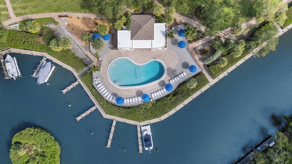 Vista aèria d'una propietat amb piscina, embarcacions amarrades i una zona enjardinada amb ombrel·les.