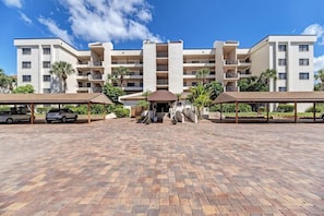 A multi-story hotel with a central entrance, covered parking, and surrounding greenery.