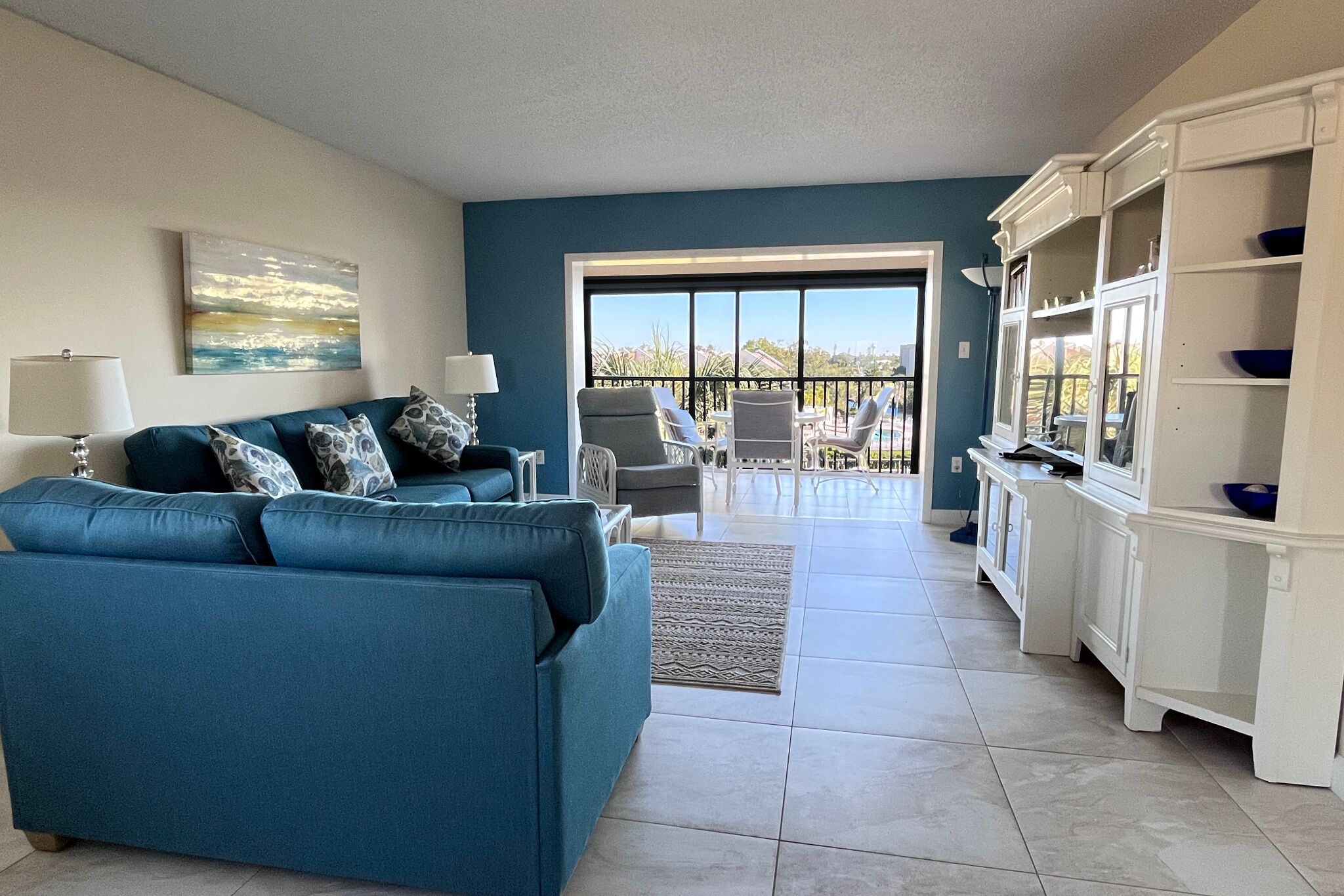 A living room with a blue sofa, a dining area with white cabinets, and a view through a glass door.