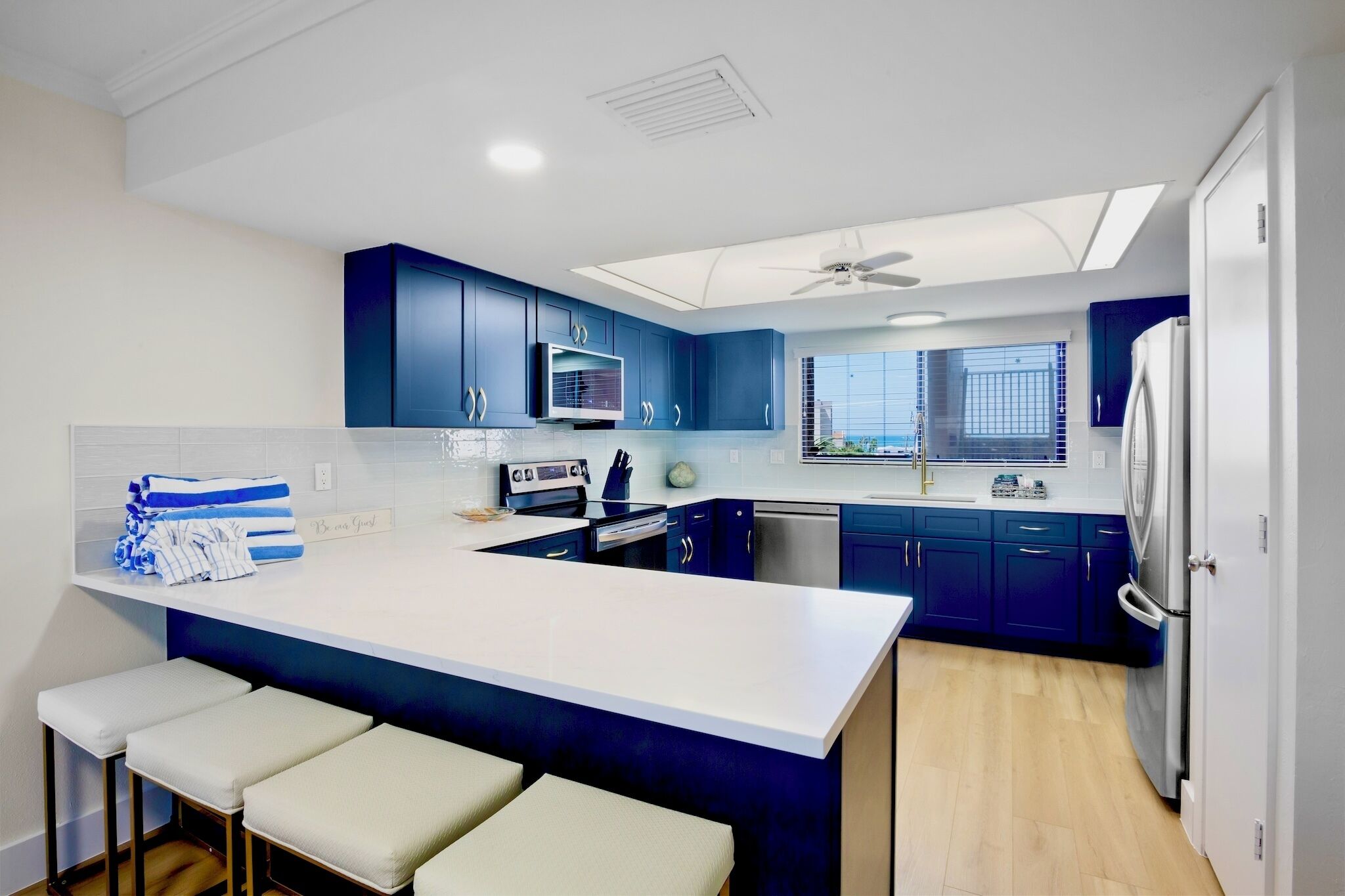 A modern kitchen with a central island, blue cabinets, white countertops, and a built-in oven.