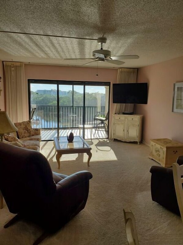Relax in this spacious living room with a sofa, chair, and flat-screen TV, plus a balcony accessible through a sliding glass door.