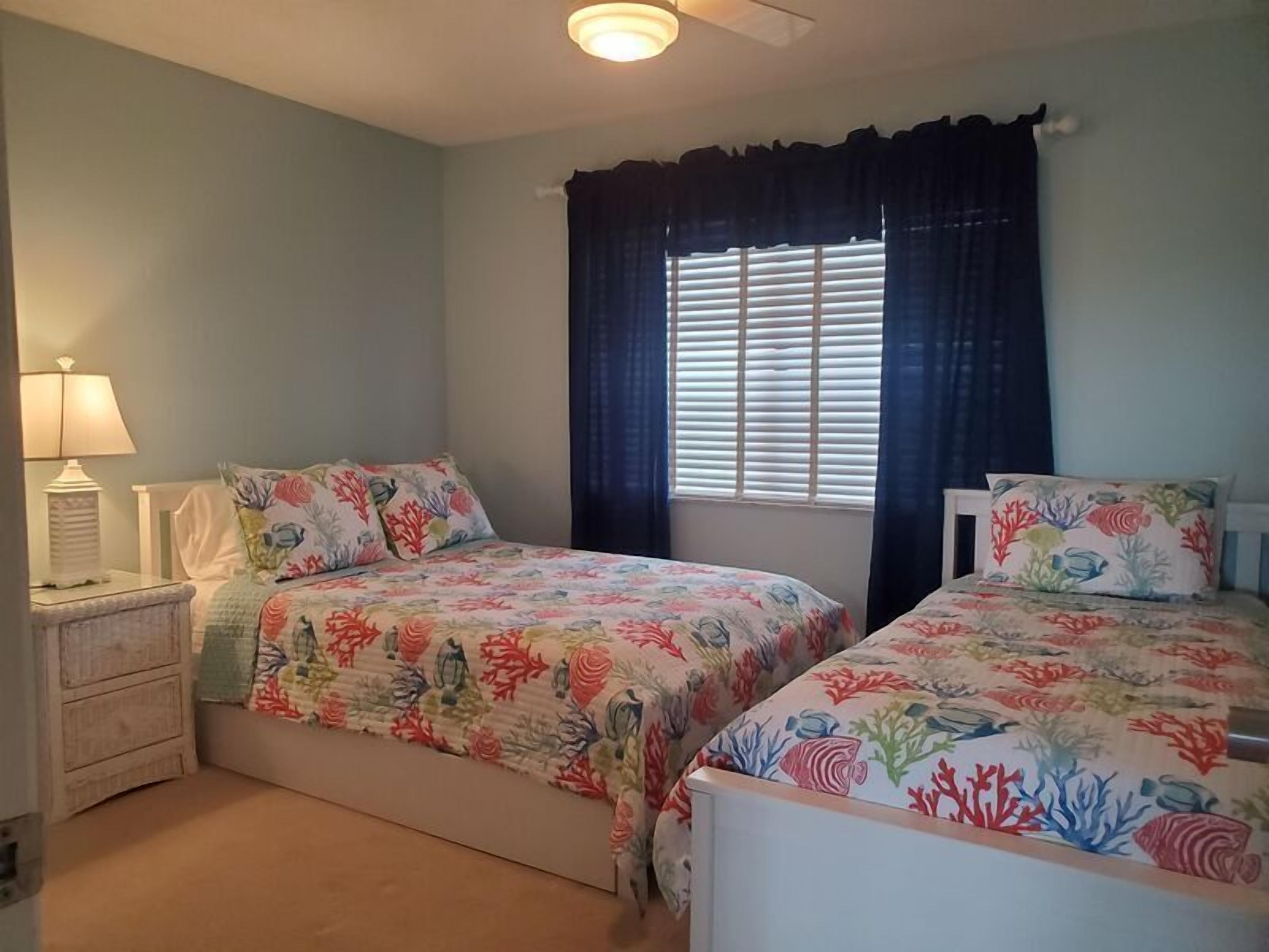 A bedroom with two beds, a nightstand, a lamp, and a window with blinds.