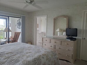 Une chambre à coucher comprenant un lit, une commode, un miroir, une télévision et donnant sur l’extérieur.