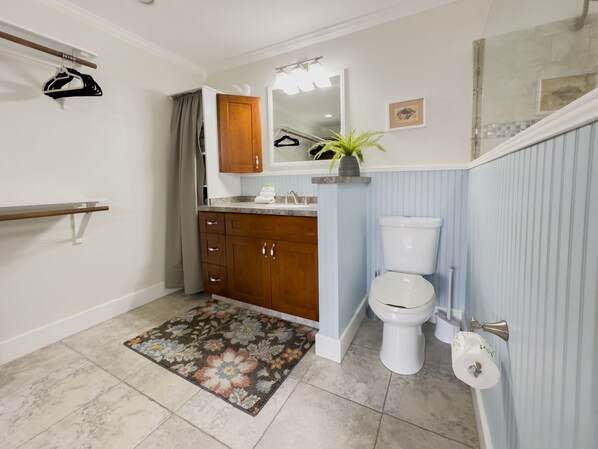 Un baño con un mueble de madera, un inodoro, un espejo, una cortina de ducha y un tapete floral.