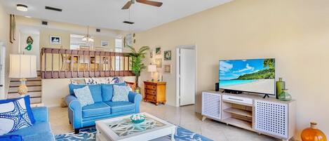 A living room with a blue sofa, a white coffee table, a TV, and a ceiling fan.