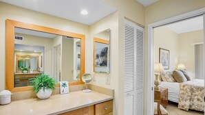 A hotel room with a large mirror, a potted plant, a bedside table, a lamp, and a bed with a floral bedspread. - Our House at the Beach C-112 Great Location, Spacious, Updated (Siesta Key)