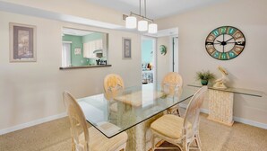 A dining area with a glass-top table, four chairs, a wall clock, and a small potted plant.