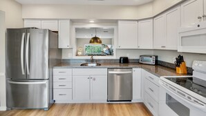 A modern kitchen with white cabinetry, stainless steel appliances, a granite countertop, and a built-in oven. - Our House at the Beach C-214 Quiet Location, newly updated (Siesta Key)