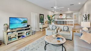 A modern living room with a flat-screen TV, a sofa, a coffee table, and a staircase leading to an upper level. - Our House at the Beach C-214 Quiet Location, newly updated (Siesta Key)